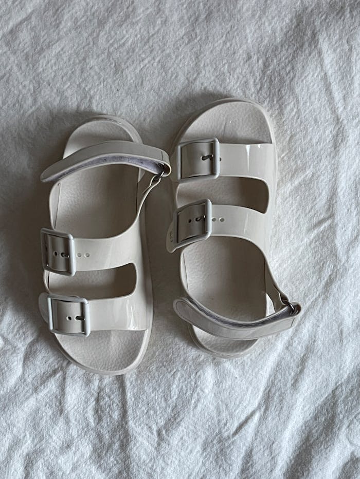 services-04 Minimalist white sandals with buckles on a textured white fabric surface.
